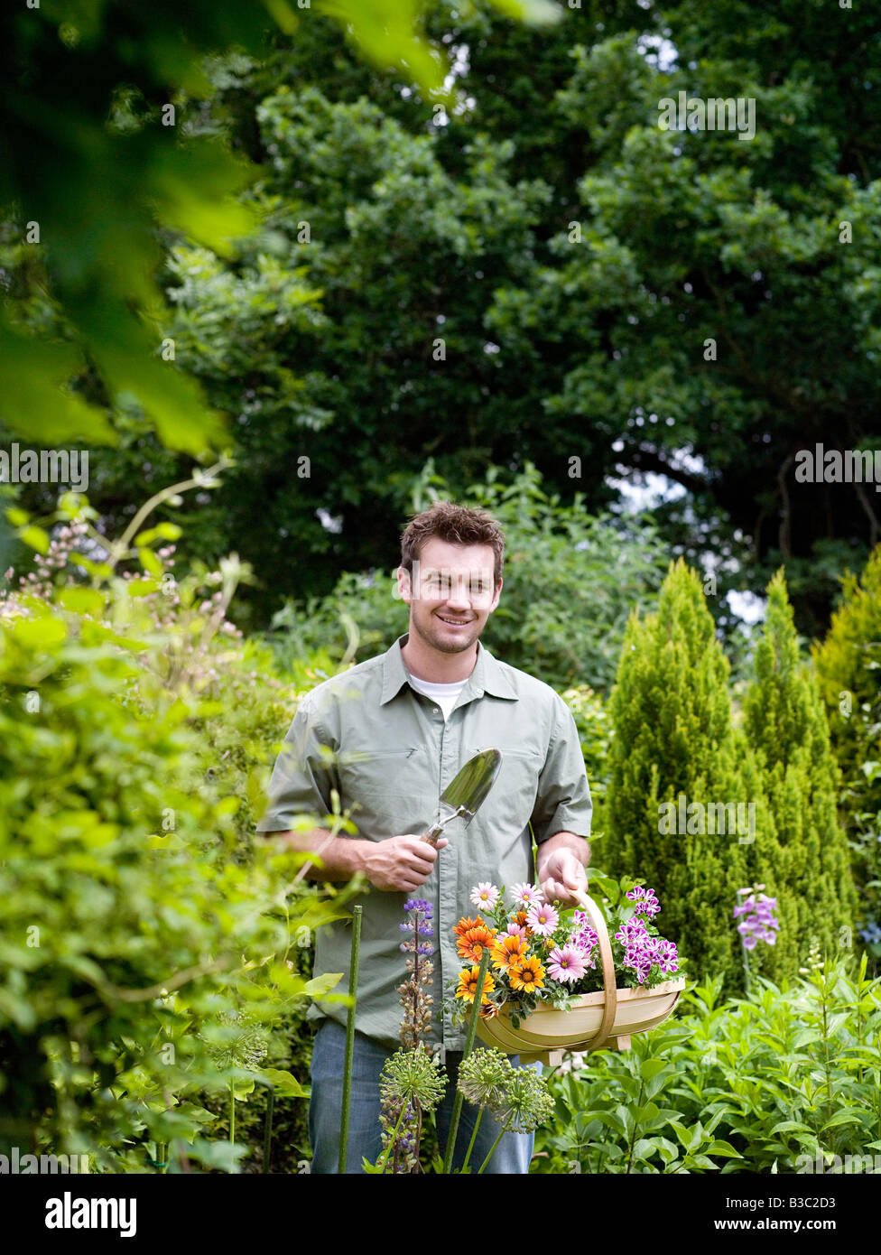 A Mann stand mit Blumen und Kelle im Garten Stockfoto