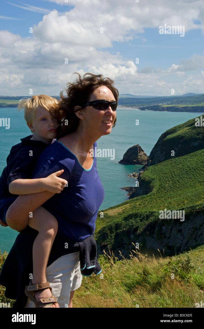 England, Wales, Pembrokeshire. Eine Mutter trägt ihr kleiner Sohn entlang der Dinas Head-Bereich des Pembrokeshire Küstenweg mit Blick in Richtung Nadel Rock und Newport Bay jenseits. (MR). Stockfoto