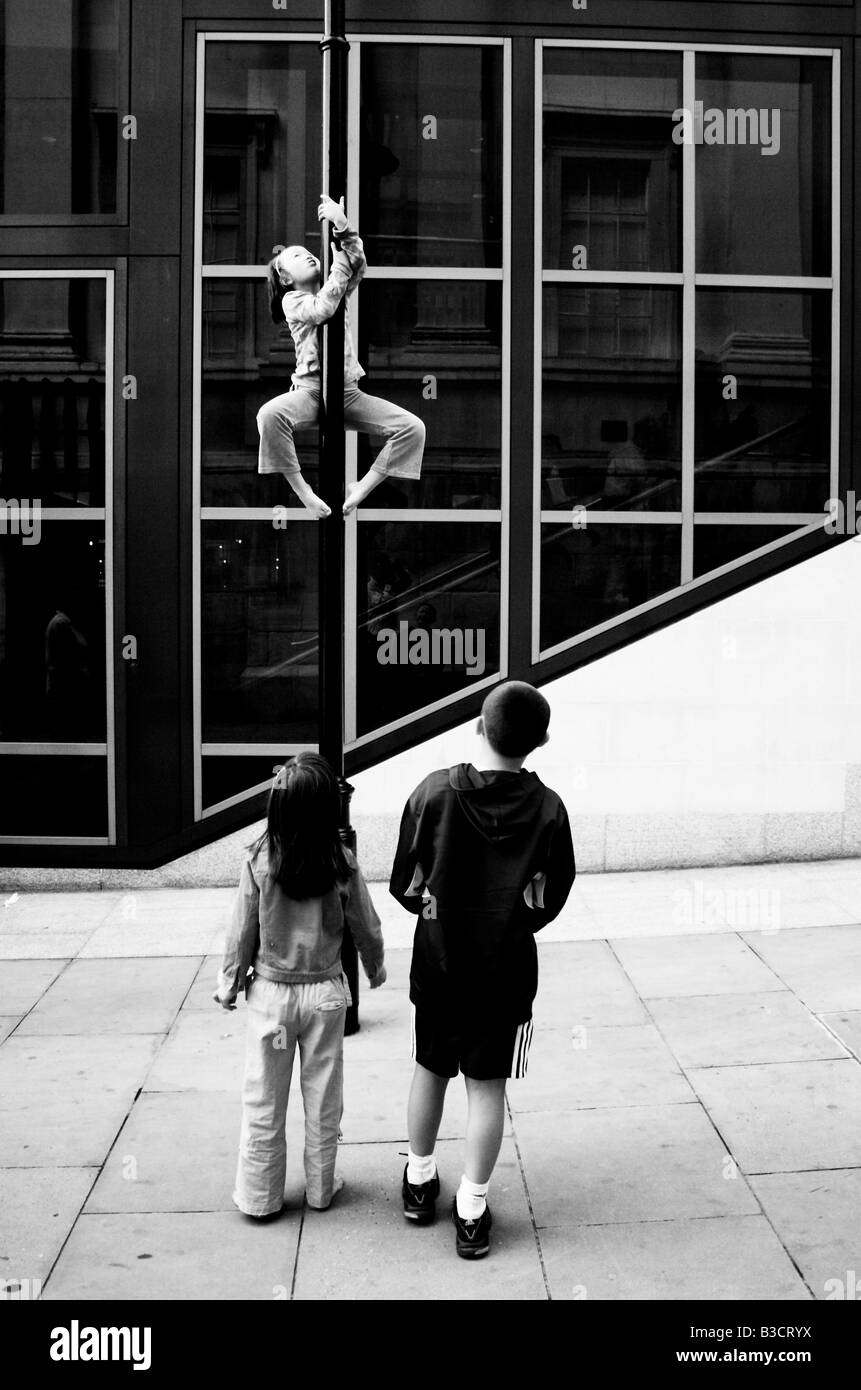 drei Kinder spielen in der Straße, zentrales London. Man klettert einen Laternenpfahl, beobachtet von ihren Freunden Stockfoto