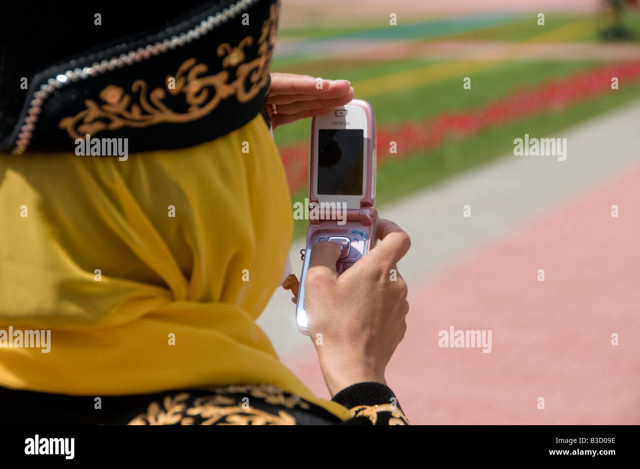 Frau in traditioneller Kleidung, die mit einem alten Handy Fotos gemacht hat. Kasachstan Stockfoto