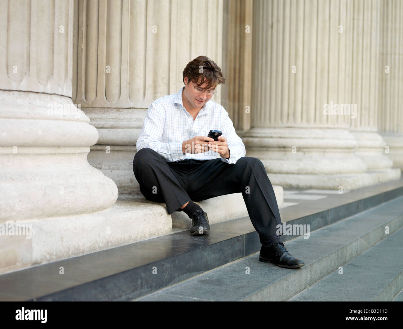 Ein Geschäftsmann Überprüfung sein Handy unter den europäischen Stil Pfeiler und Säulen in London, England. Stockfoto