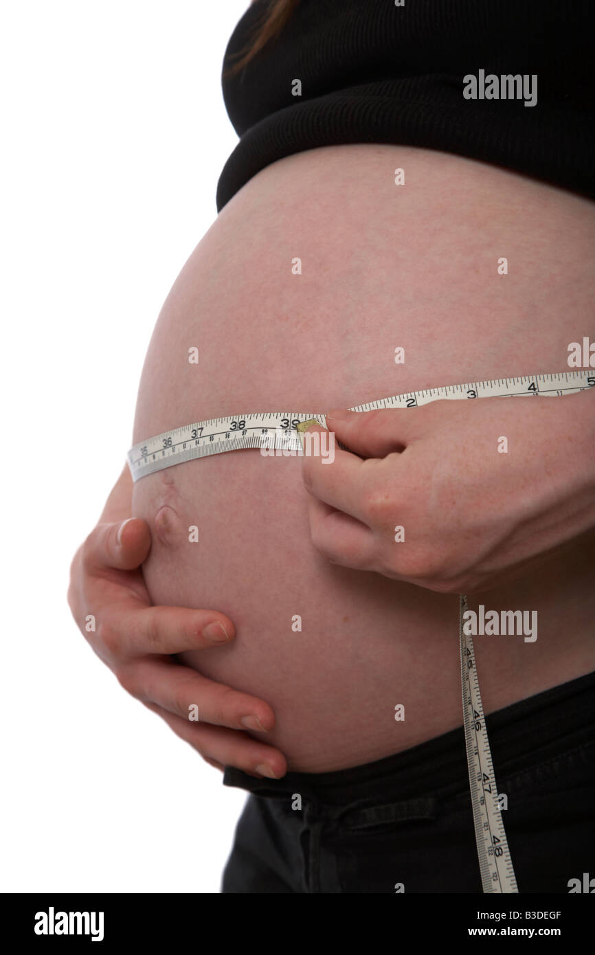 Nahaufnahme von 8 Monat schwanger, Mitte der zwanziger Jahre Frau 25 Jahre alt, die Messung der Babybauch mit Maßband mit Zoll und Metri Stockfoto