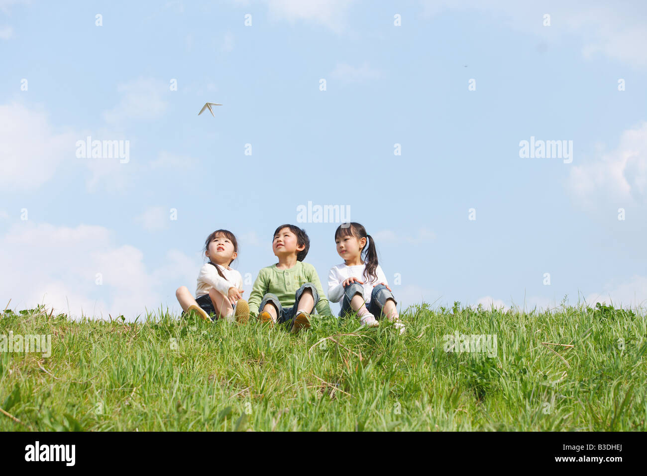 Kinder im Park sitzen und mit Blick auf fliegende Papierflieger Stockfoto