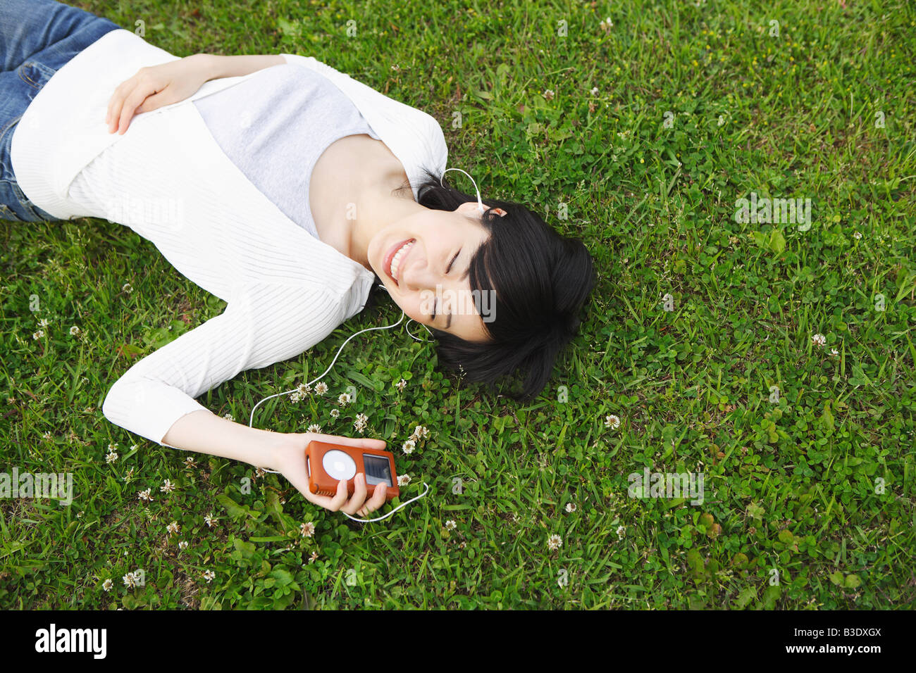 Junge Frau auf dem Rasen liegen und Musik hören Stockfoto