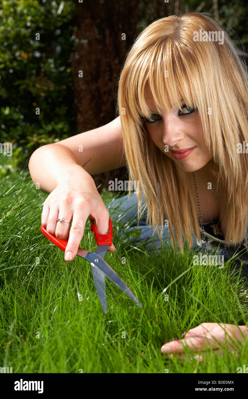 junge blonde behaarte Frau späten Teenager Anfang zwanzig schneiden Rasen in einem Garten mit einer Schere Stockfoto