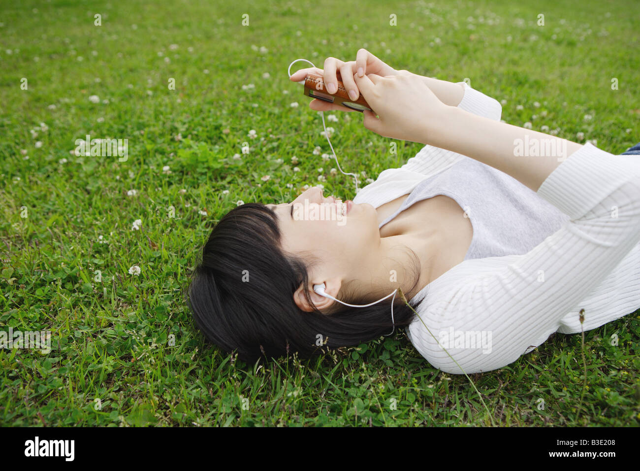 Junge Frau auf dem Rasen liegen und Musik hören Stockfoto