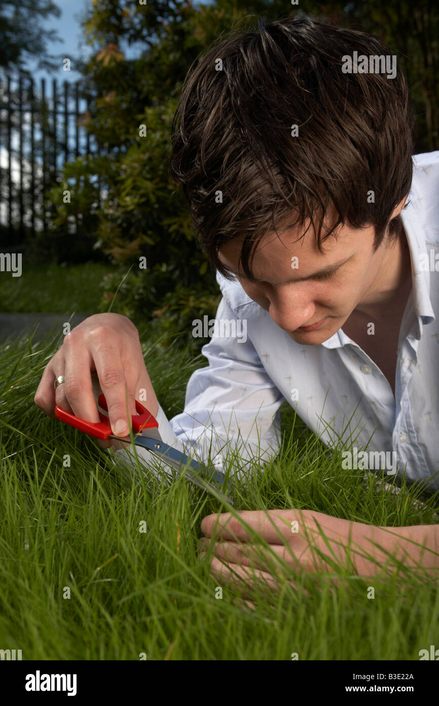 junge dunkelhaarig Mann späten Teenager Anfang zwanzig schneiden mit der Schere in einem Garten Rasen Stockfoto