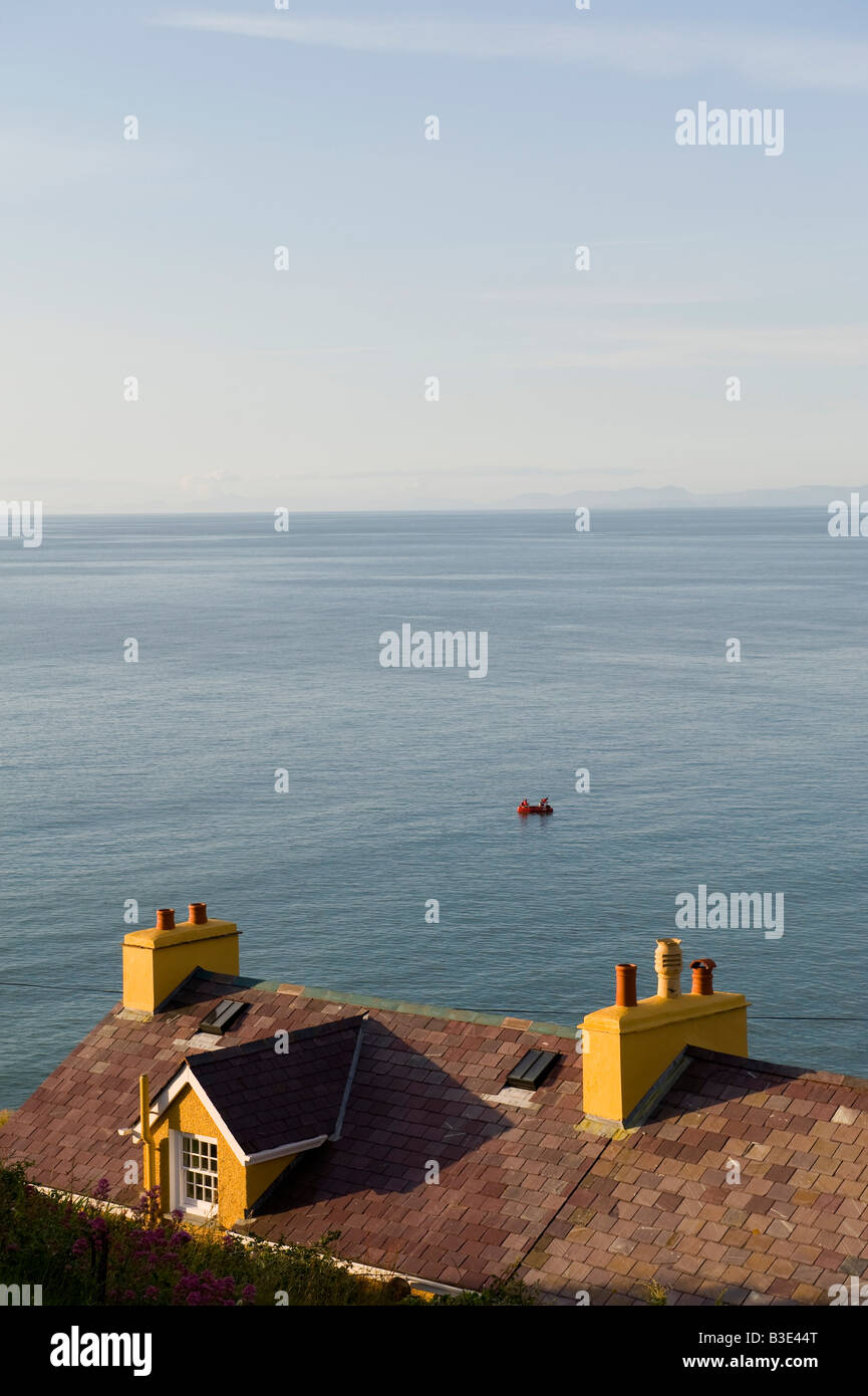 New Quay, Wales. Ein Blick über die Dächer der Stadt zum Meer mit zwei Männern, die friedlich von einem kleinen Schlauchboot aus angeln Stockfoto