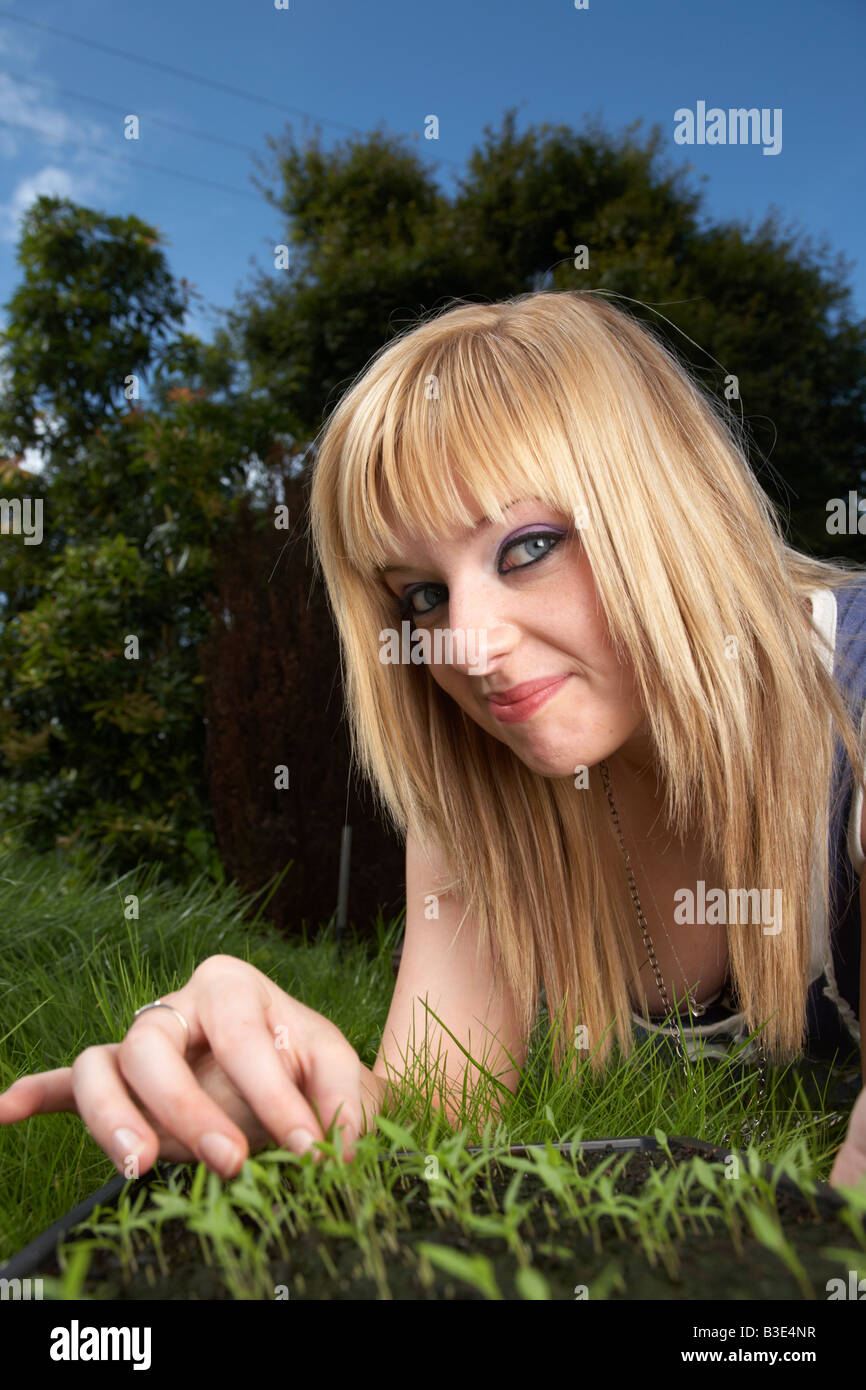 junge blonde behaarte Frau späten Teenager frühen zwanziger Jahren tendenziell ein Tablett mit Petersilie Kraut Sämlinge in einem Garten Stockfoto