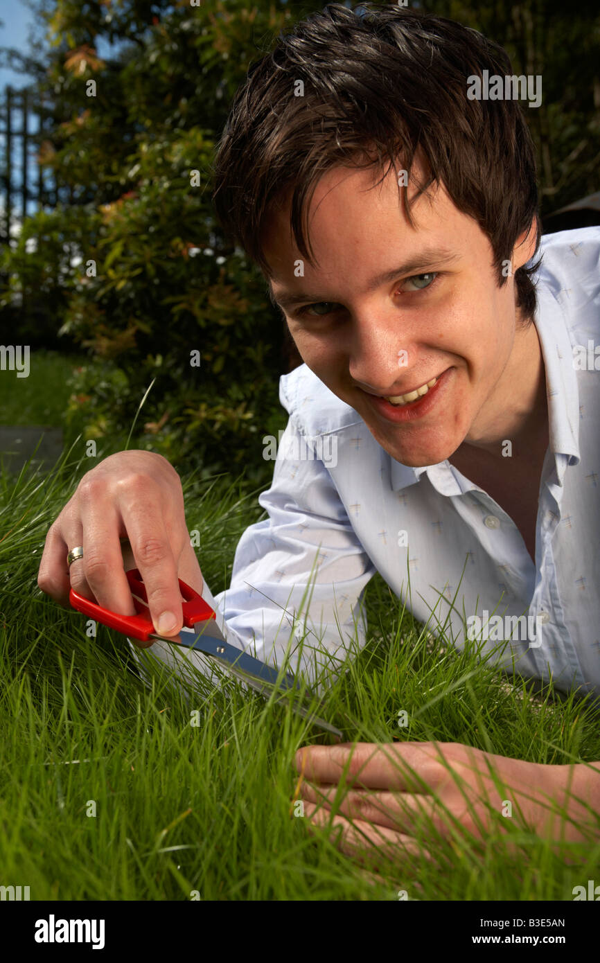 junge dunkelhaarig Mann späten Teenager Anfang zwanzig schneiden mit der Schere in einem Garten Rasen Stockfoto