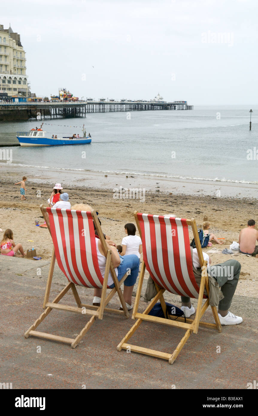 Ein paar saß in Liegestühlen mit Blick auf Llandundo Strand und pier Stockfoto