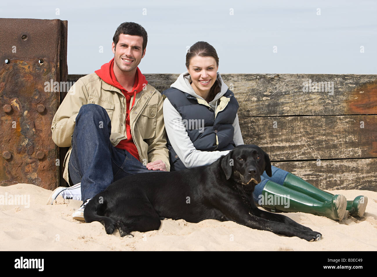 Paar mit Hund am Strand sitzen Stockfoto