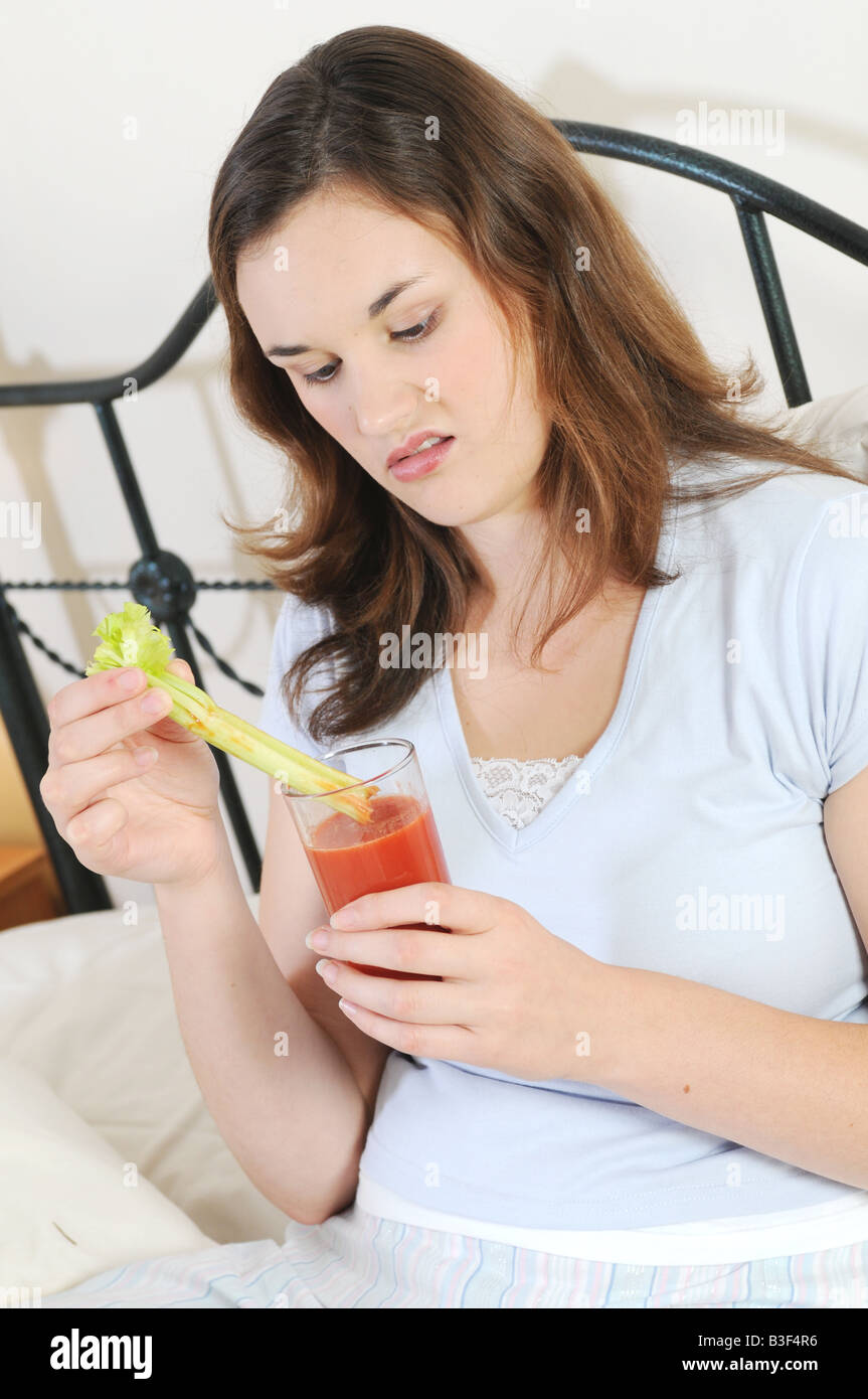 ein Mädchen einen Tomatensaft trinken, im Bett schauen angewidert Stockfoto