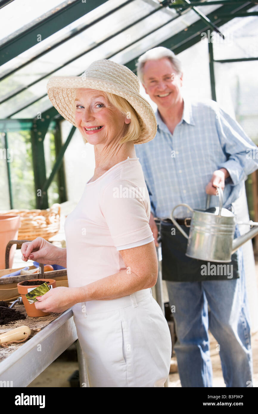 Frau im Gewächshaus Pflanzen, Samen und Mann mit Gießkanne lächelnd Stockfoto
