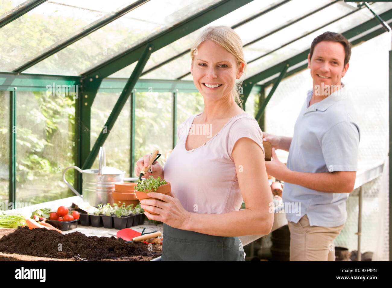 Paar im Gewächshaus Boden in Töpfen lächelnd Rechen Stockfoto