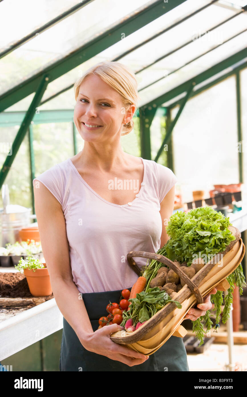 Frau im Gewächshaus halten Korb mit Gemüse lächelnd Stockfoto