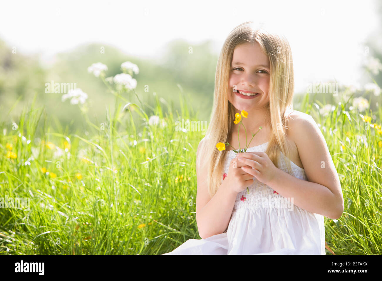 Junges Mädchen sitzen im Freien halten lächelnde Blume Stockfoto