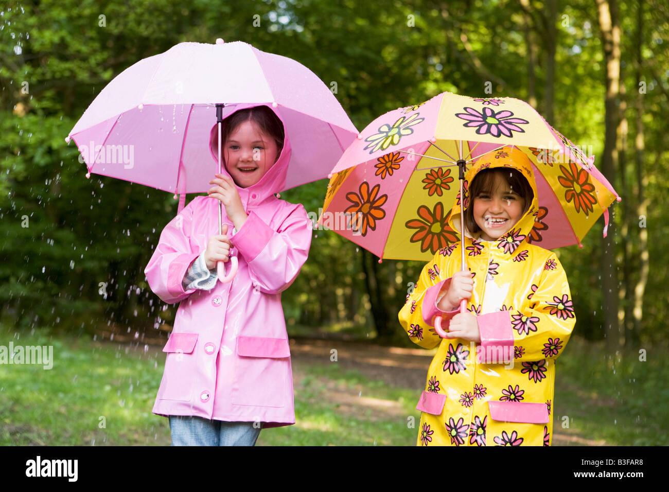 Zwei Schwestern im Freien bei Regen mit Sonnenschirmen lächelnd Stockfoto