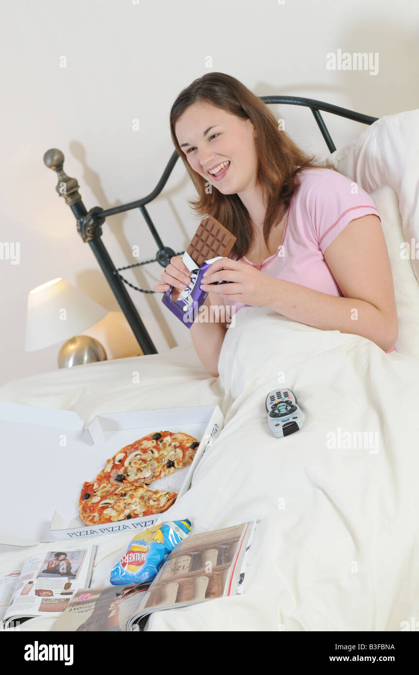 ein Mädchen im Bett vor dem Fernseher Junkfood Essen Stockfoto