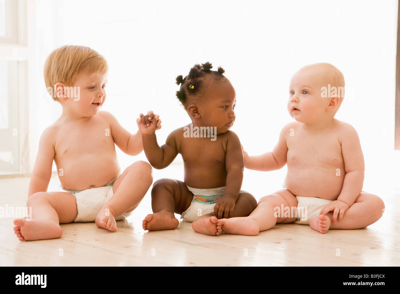 Drei Babys sitzen drinnen Hand in Hand Stockfoto