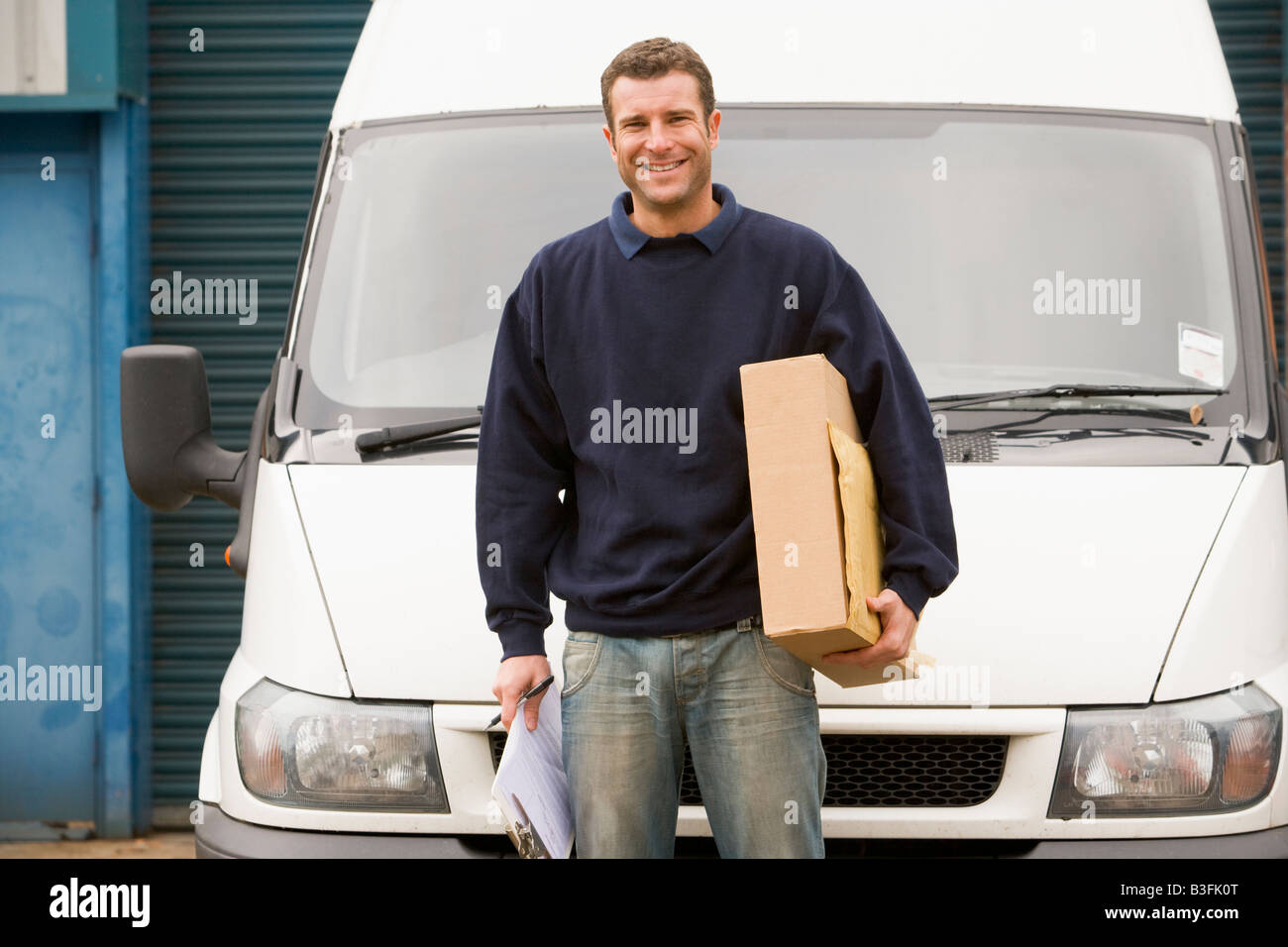 Deliveryperson stehend mit van mit Zwischenablage und ein Lächeln auf den Lippen Stockfoto