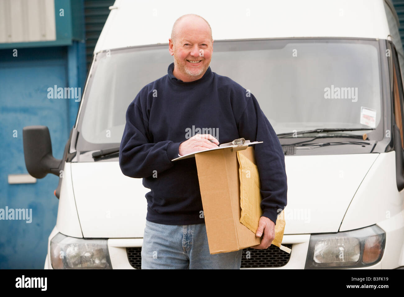 Deliveryperson stehend mit van mit Zwischenablage und ein Lächeln auf den Lippen Stockfoto