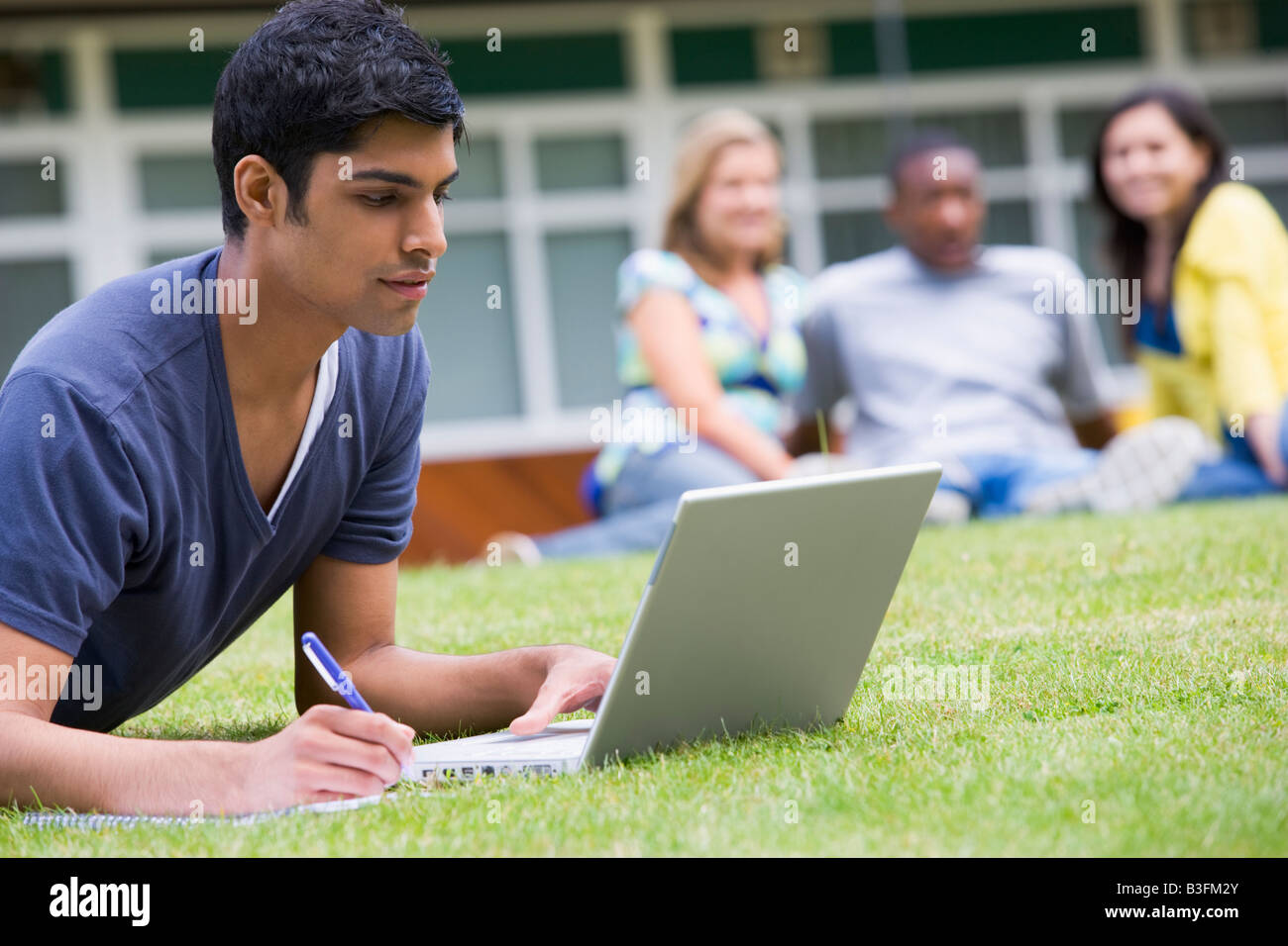 Student im Freien auf Rasen mit Laptop mit anderen Studenten im Hintergrund (Tiefenschärfe) Stockfoto