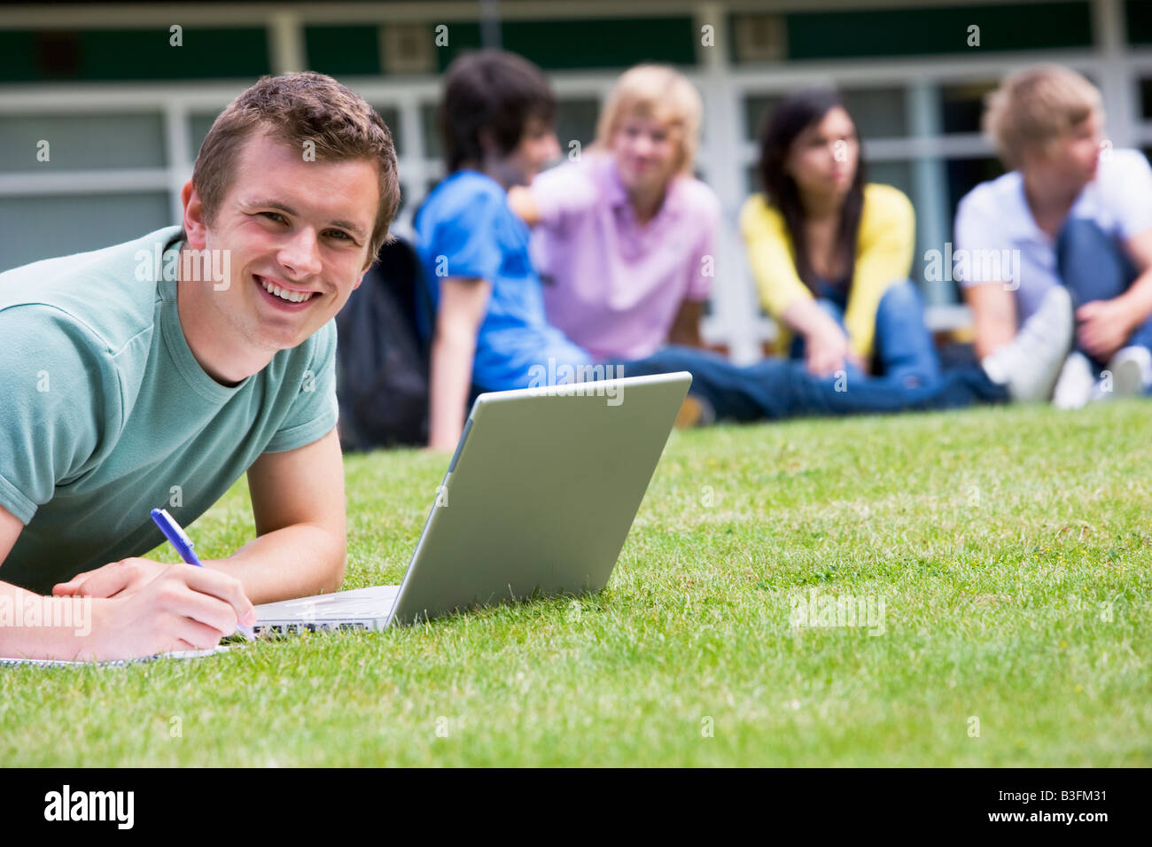 Student im Freien auf Rasen mit Laptop mit anderen Studenten im Hintergrund (Tiefenschärfe) Stockfoto