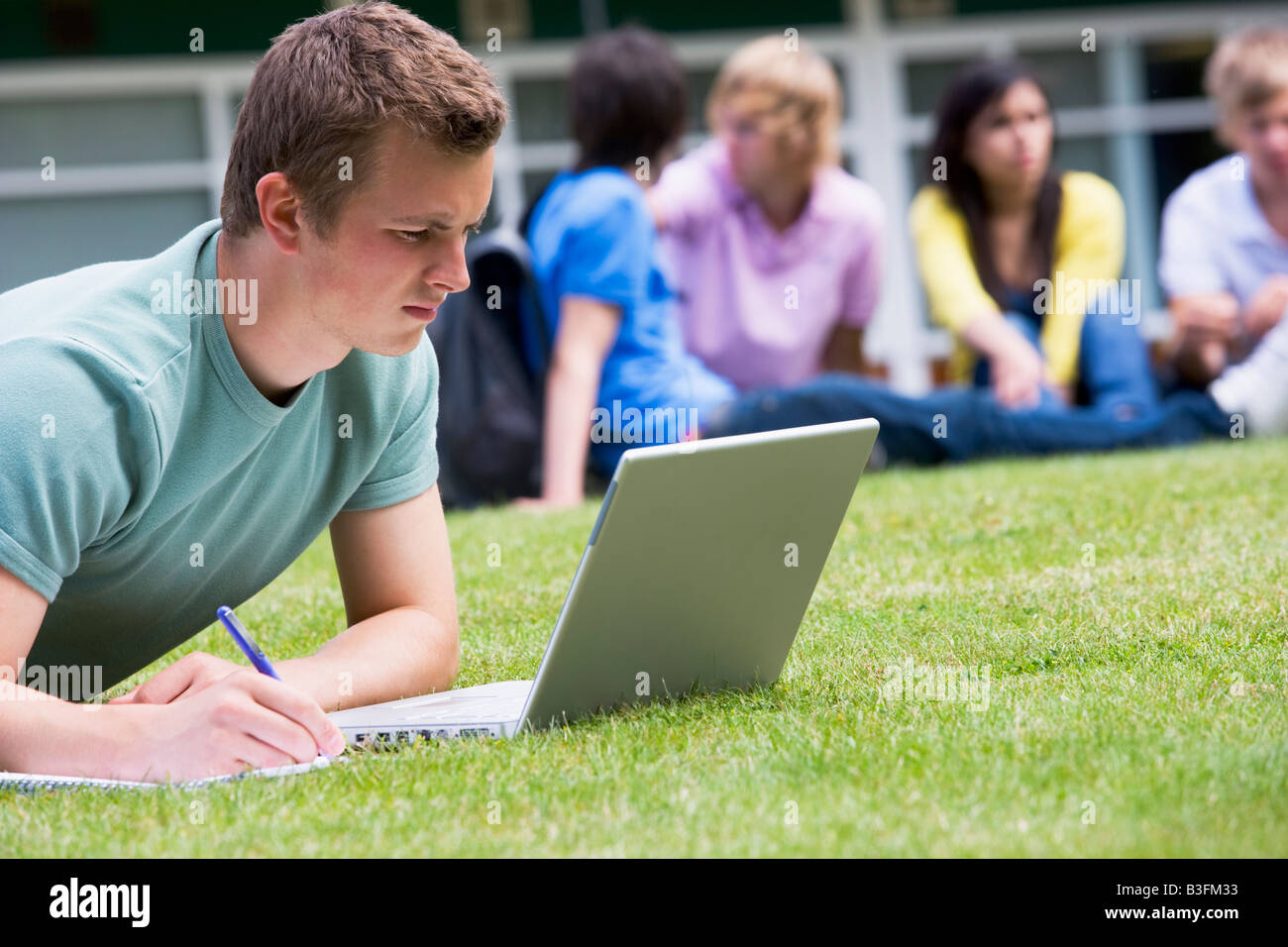 Student im Freien auf Rasen mit Laptop mit anderen Studenten im Hintergrund (Tiefenschärfe) Stockfoto
