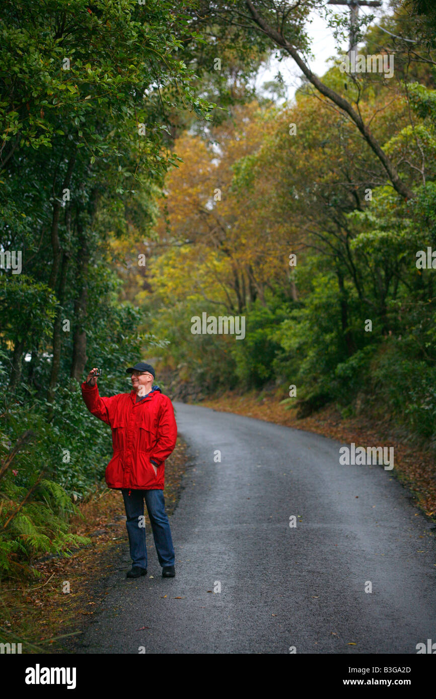 Ein Mann in einem roten Regenjacke geht auf einer Landstraße an einem verregneten Tag Stockfoto