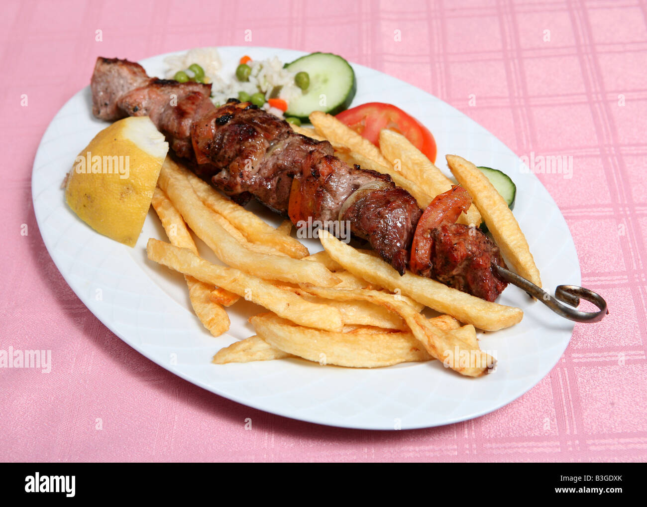 Ein Schweinefleisch Souvlaki oder Kebab serviert auf dem Spieß mit frittierten Pommes frites Reis und Gemüse Souvlaki ist eine griechische Taverne standard Stockfoto