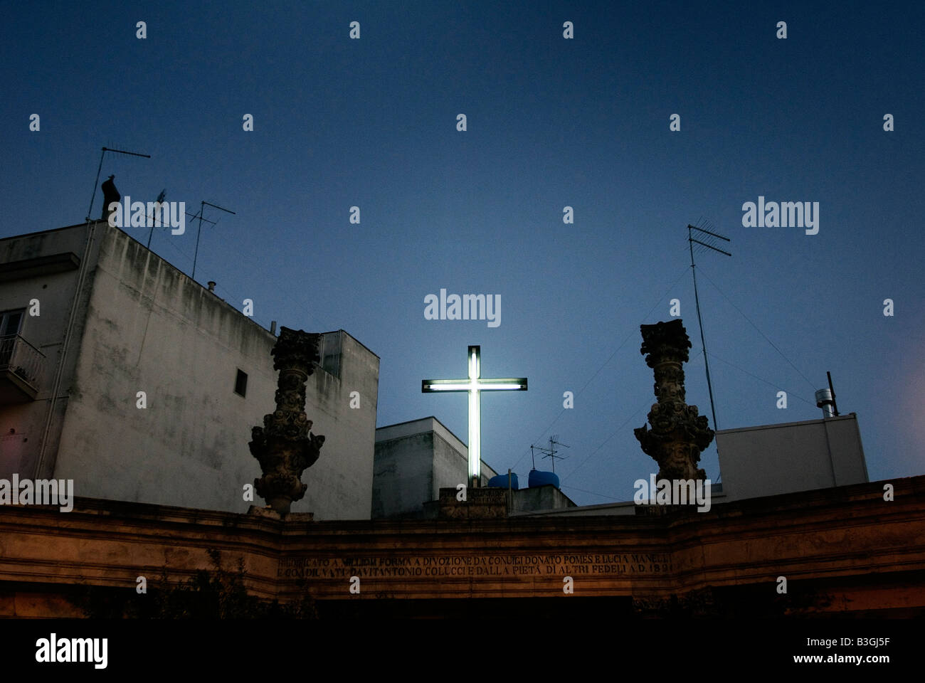 Italien, Apulien, Ostuni. Kruzifix-Licht auf dem Gebäudedach in der Nacht Stockfoto