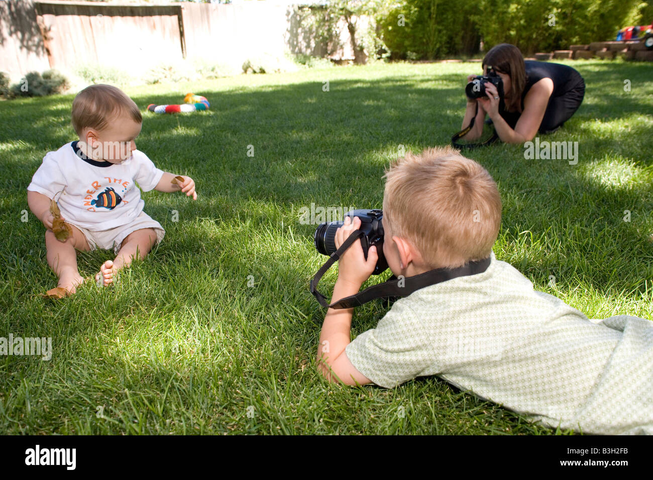 Eltern und Kind fotografieren Baby Junge sitzt im Rasen spielen mit Blättern zu Hause, Hinterhof, usa Stockfoto