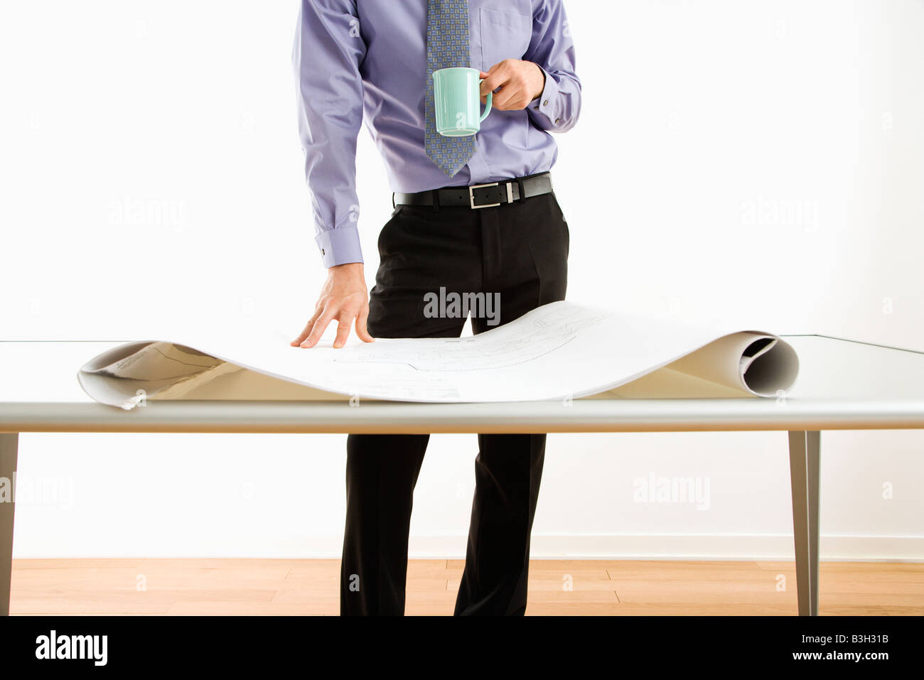 Business-Mann stehend mit Kaffeetasse neben Tisch mit Blaupausen Stockfoto