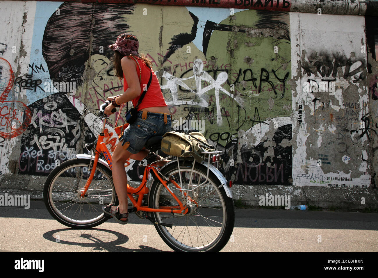 Radfahrer vorbei an Breschnew und Honecker s Kuss abgebildet auf der Berliner Mauer im East Side Gallery in Berlin, Deutschland Stockfoto