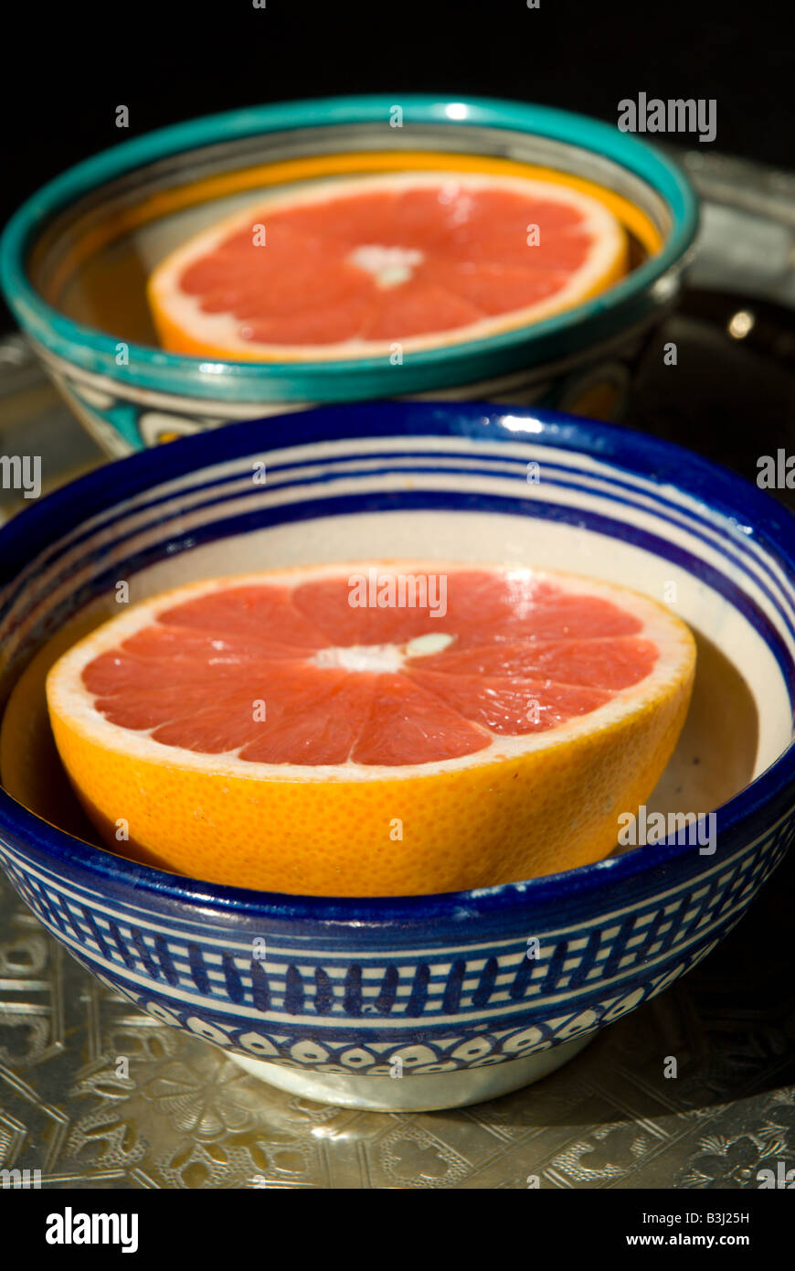 Zwei Hälften einer rosa Grapefruit in der Morgensonne in bunte marokkanische Schalen auf einem silbernen Tablett serviert. Stockfoto