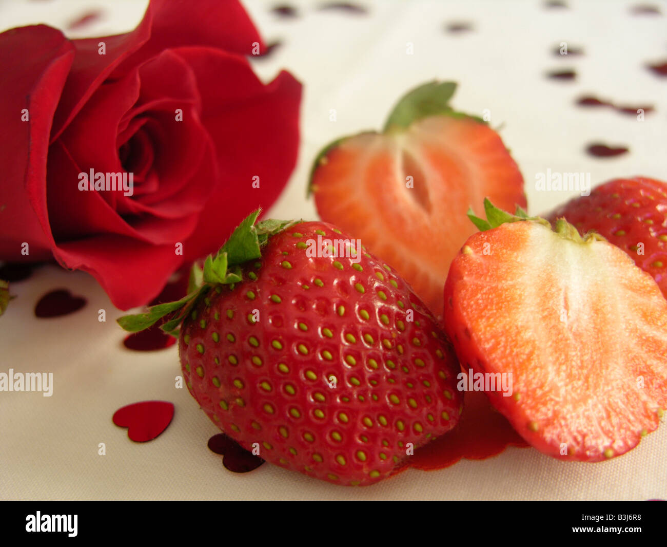 Nahaufnahme von geschnittene Erdbeeren und eine rote rose mit herzförmigen Streusel auf einem rosa Hintergrund Stockfoto