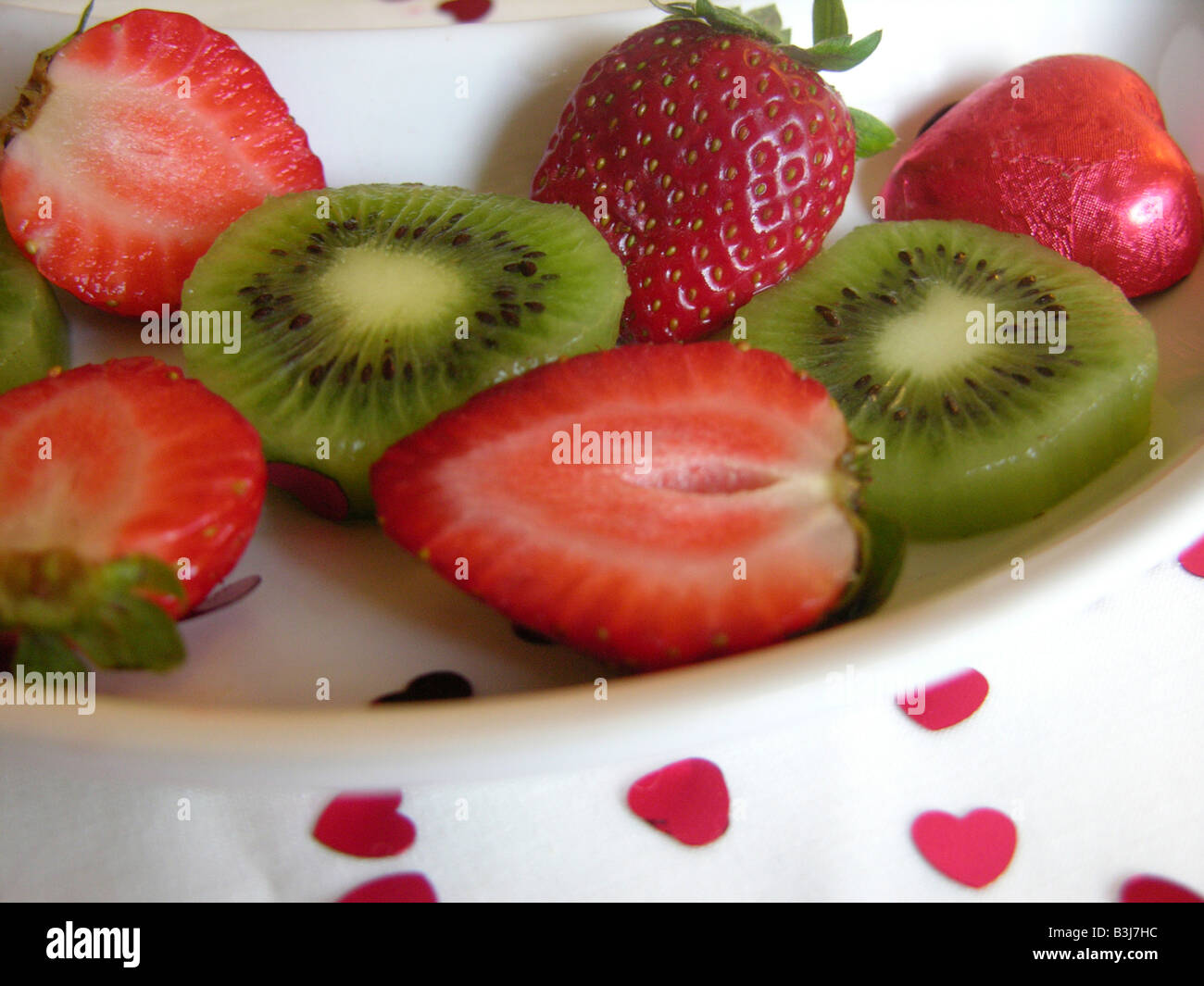 Nahaufnahme von Pralinen geschnittene Erdbeeren und Kiwis auf einem weißen Teller mit herzförmigen Streusel Stockfoto