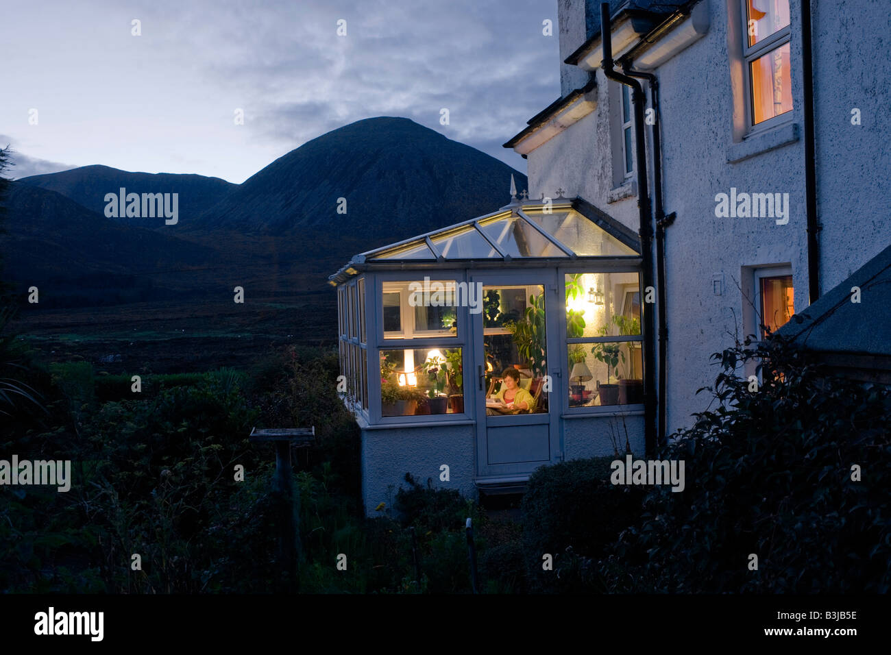 Resident des Swordale Haus befindet sich in ihrem Wintergarten der mit Blick auf Beinn Na Caillich, nr Broadford, Isle Of Skye lesen Stockfoto