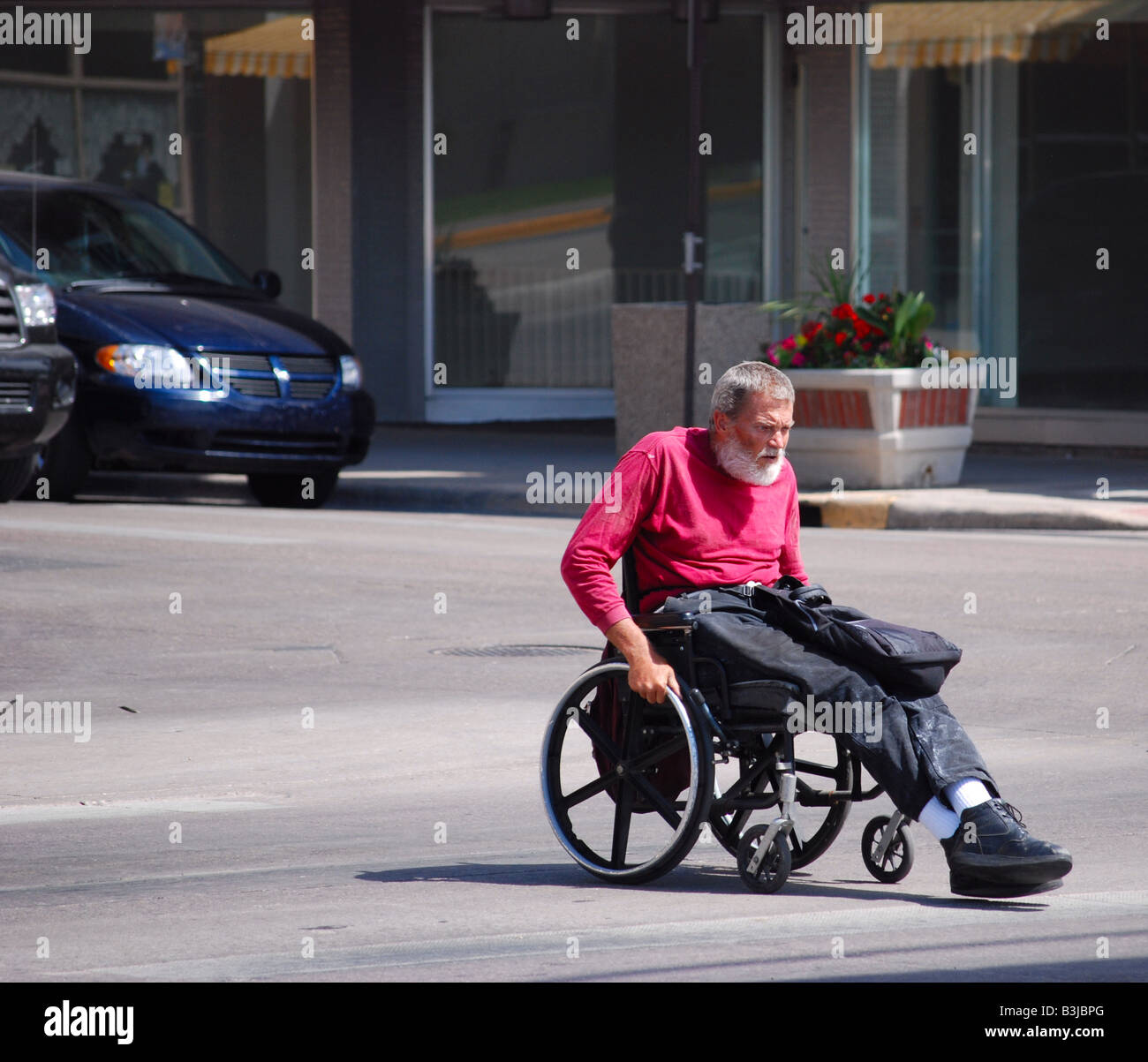 Alter Mann im Rollstuhl überqueren einer Straße Stockfoto