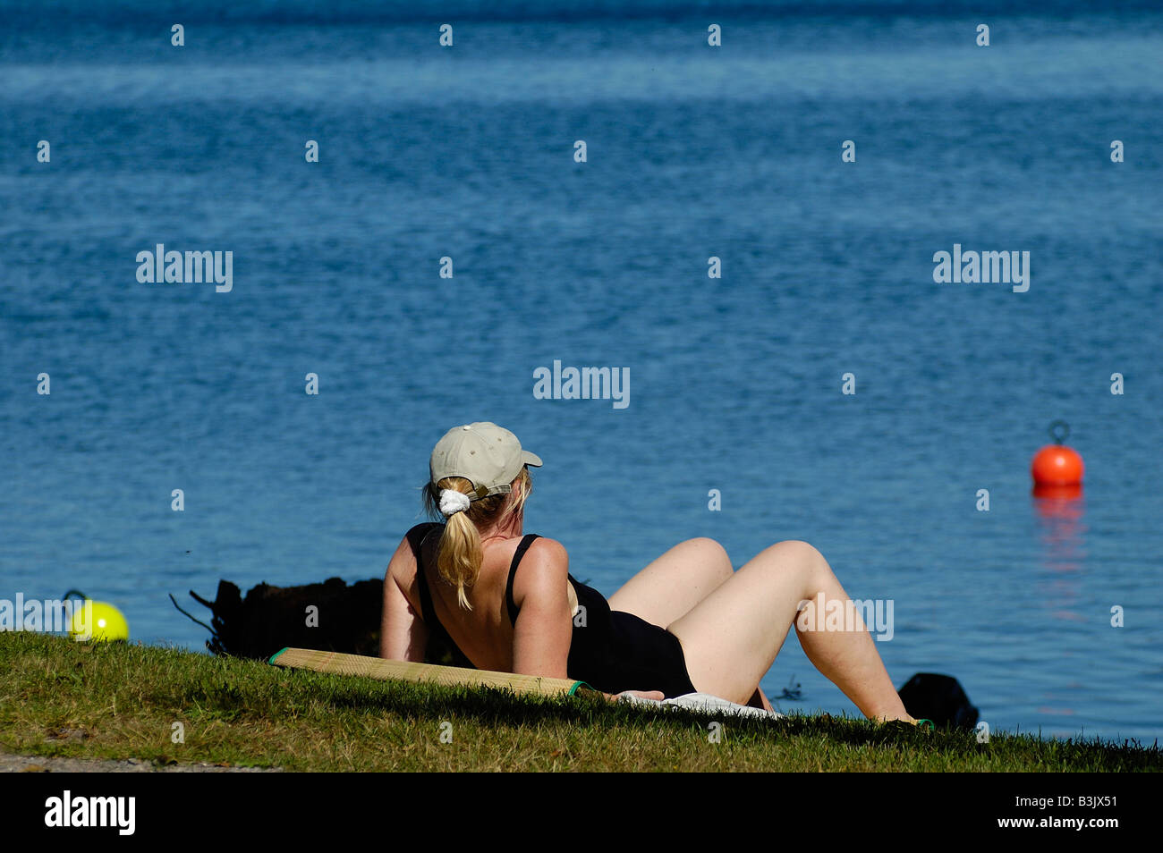 Reife Frau in schwarzen Badeanzug, genießen Sie die Sonne an bank Og einen schwedischen See Stockfoto
