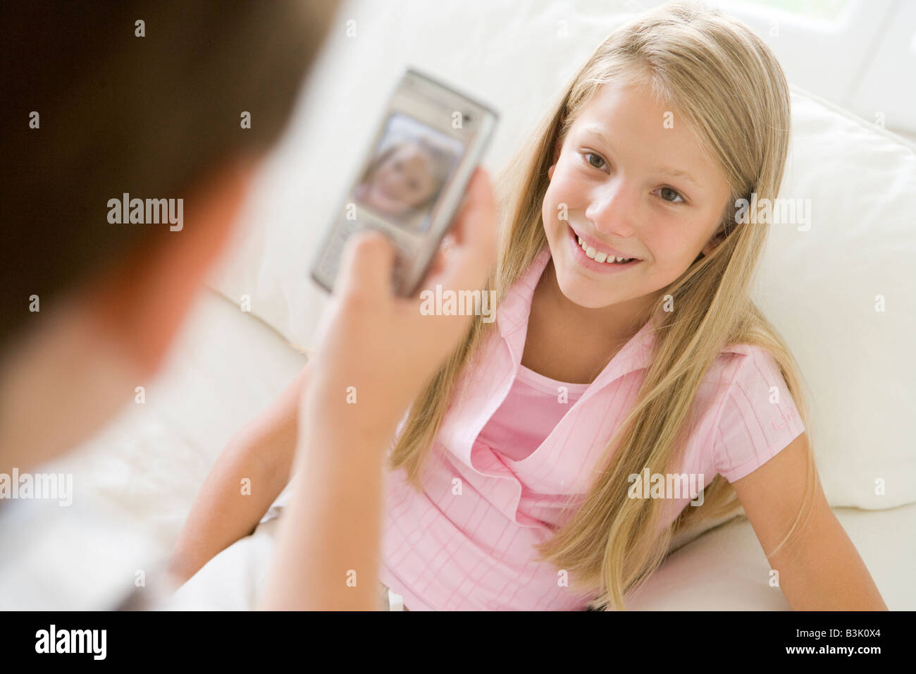 Kleiner Junge unter Bild lächelnden jungen Mädchens mit Kamera-Handy im Innenbereich Stockfoto