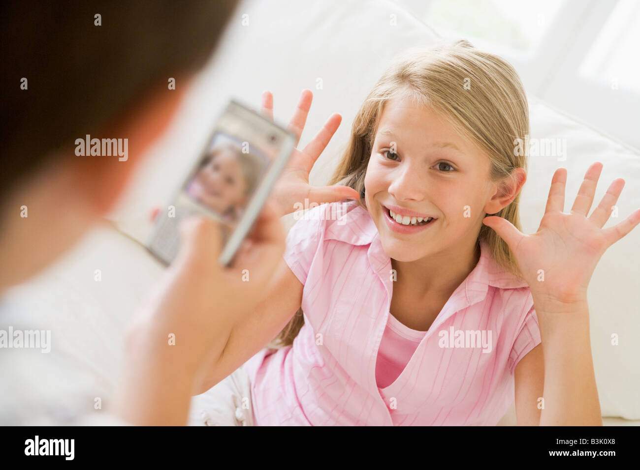 Kleiner Junge unter Bild lächelnden jungen Mädchens mit Kamera-Handy im Innenbereich Stockfoto