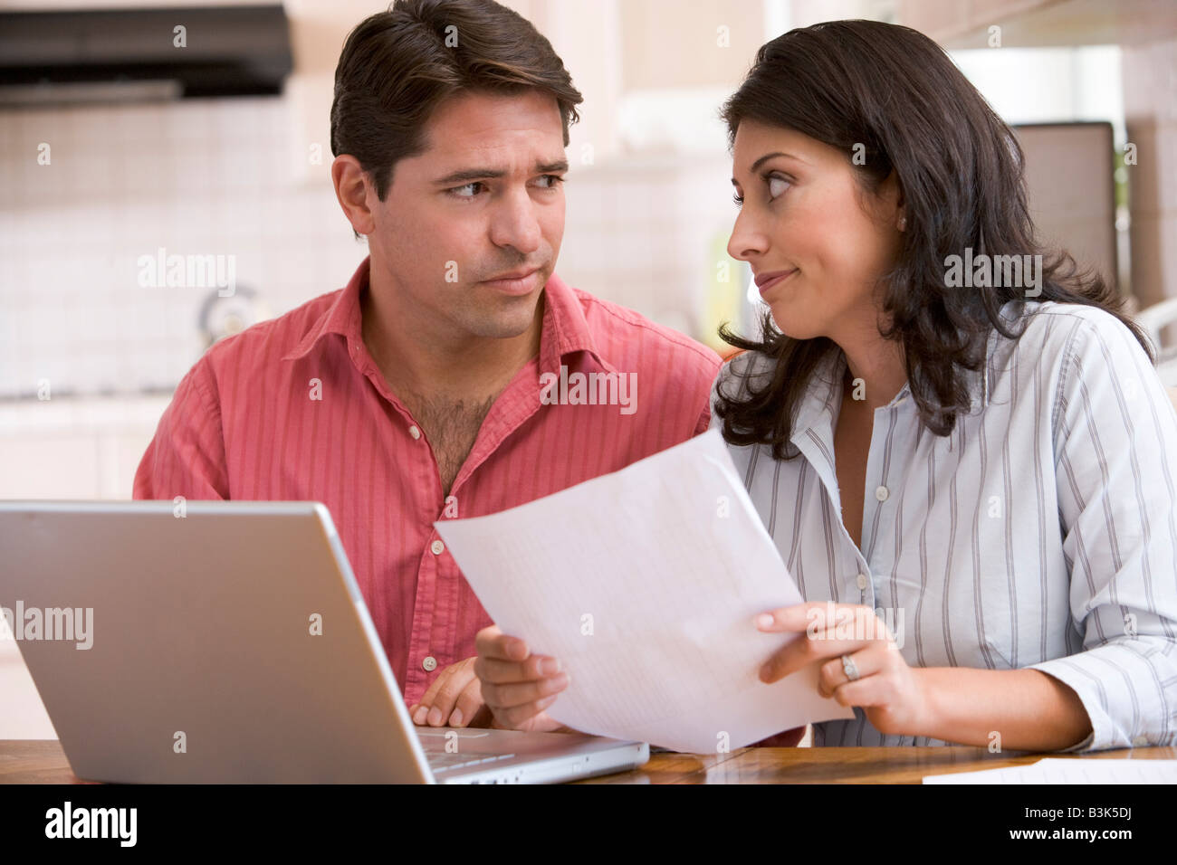Paar in der Küche mit Papierkram mit Laptop auf der Suche unglücklich Stockfoto