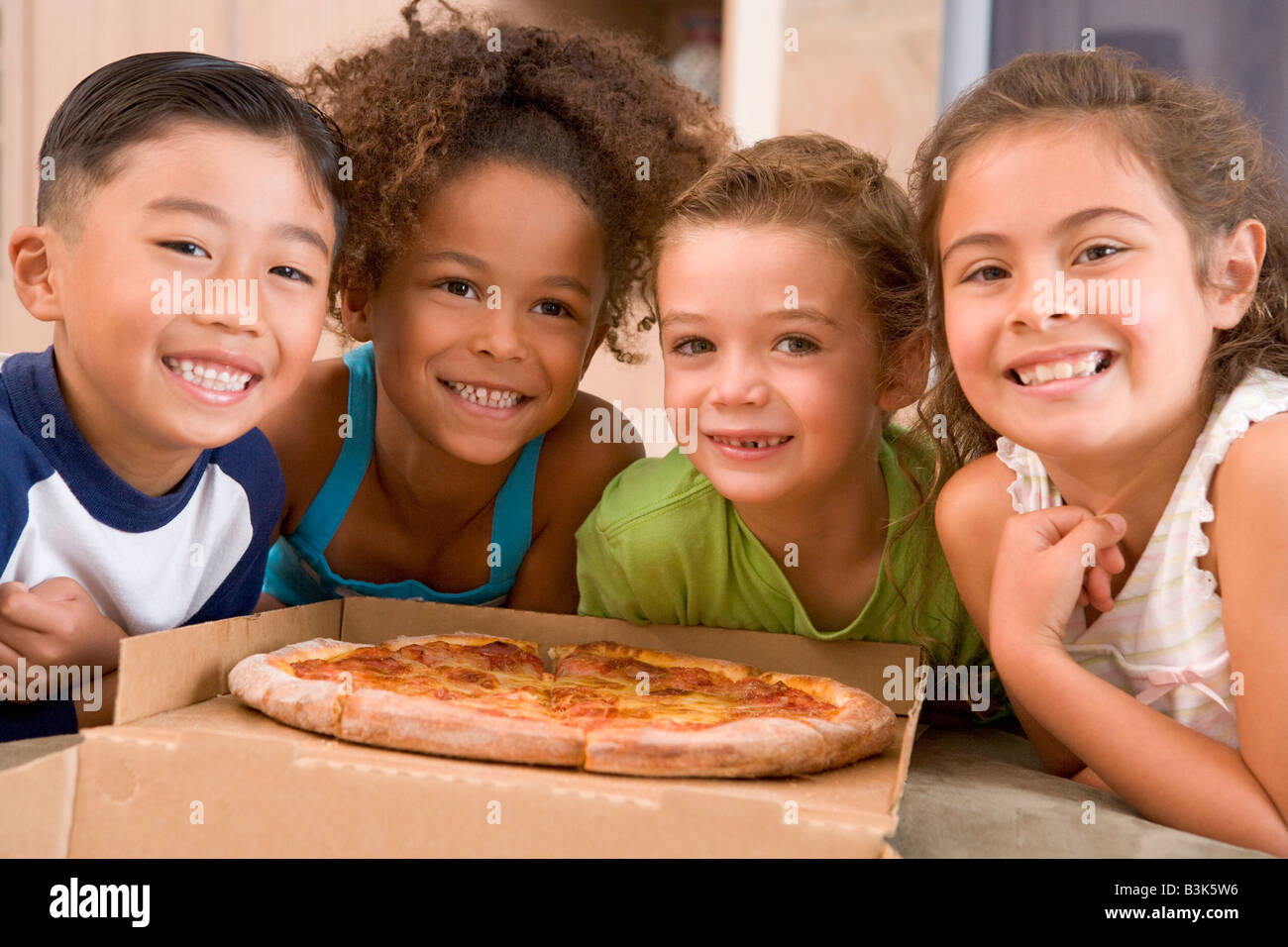 Vier kleine Kinder im Haus mit Pizza lächelnd Stockfoto