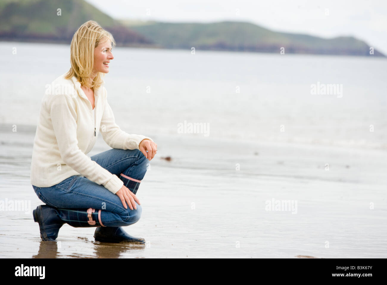 Frau am Strand lächelnd hocken Stockfoto