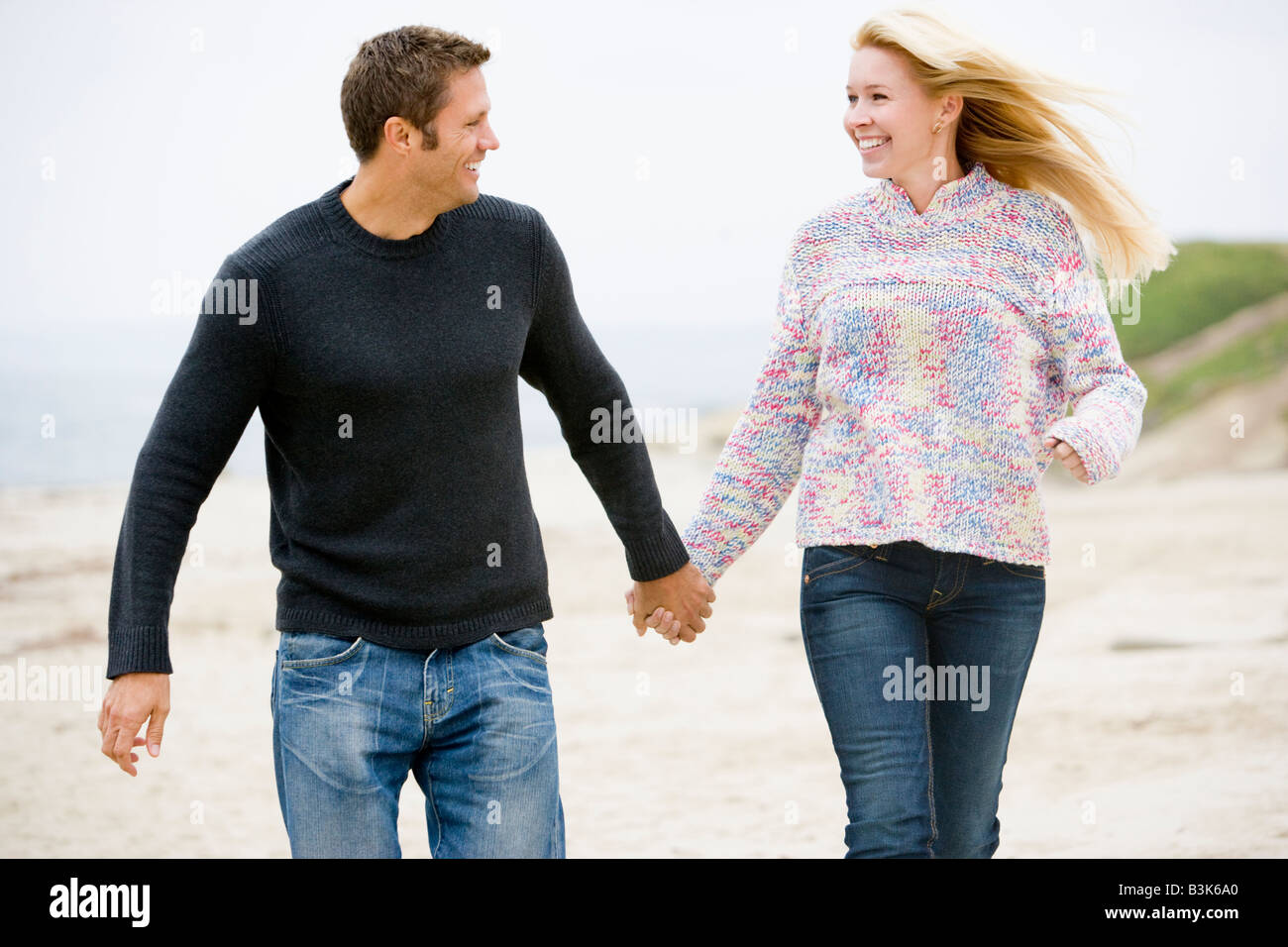 Paare, die am Strand Hand in Hand lächelnd Stockfoto