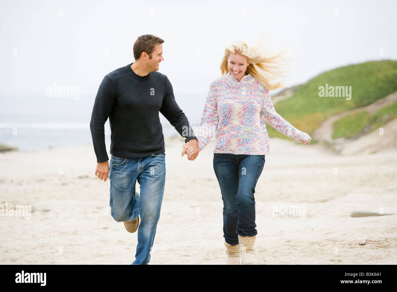 Paar am Strand, die Hand in Hand lächelnd ausgeführt Stockfoto