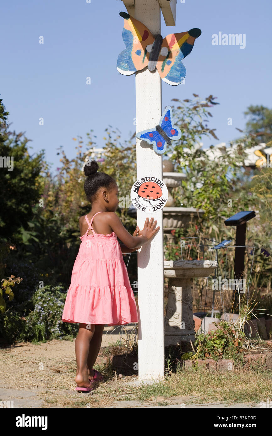 Eine Mischrasse kleines Mädchen inspiziert das "Pestizid freie" Marienkäfer Schild an einer organischen einheimische Pflanze Garten. Stockfoto