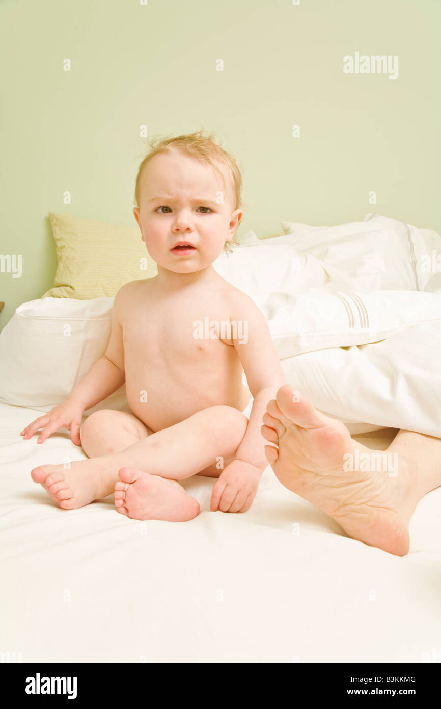 Neugierig Baby sitzt neben Mutters Füßen im Bett Stockfoto